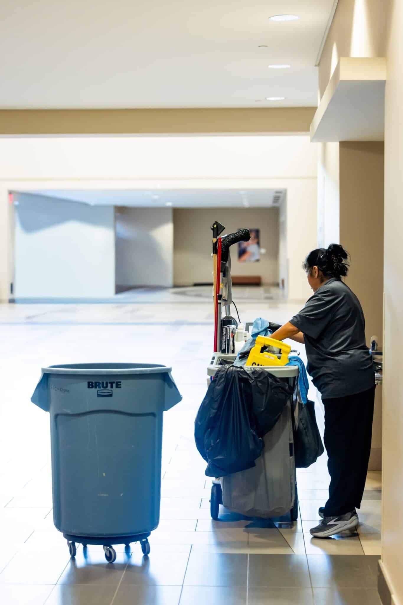 Janitorial worker with cleaning cart in a large commercial hallway